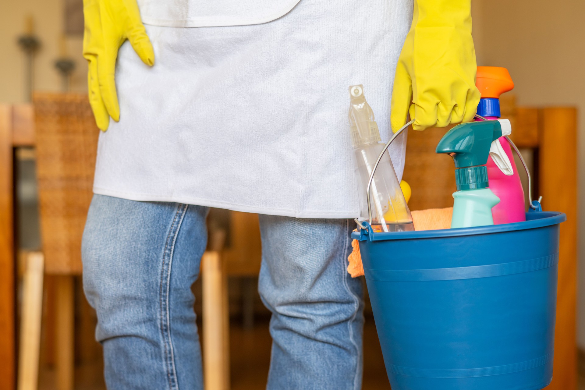 Professional Home Cleaning Worker Wearing Gloves Holding Blue Bucket With Cleaning Products And Spray Bottles For Thorough Household Sanitation And Efficient Dust Removal In Residential Environment